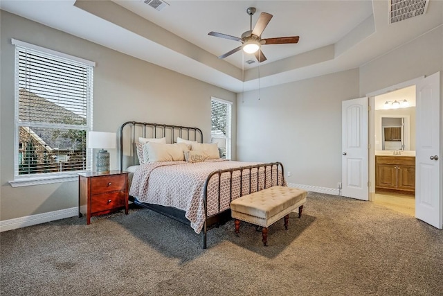 carpeted bedroom featuring a raised ceiling, ceiling fan, sink, and ensuite bath