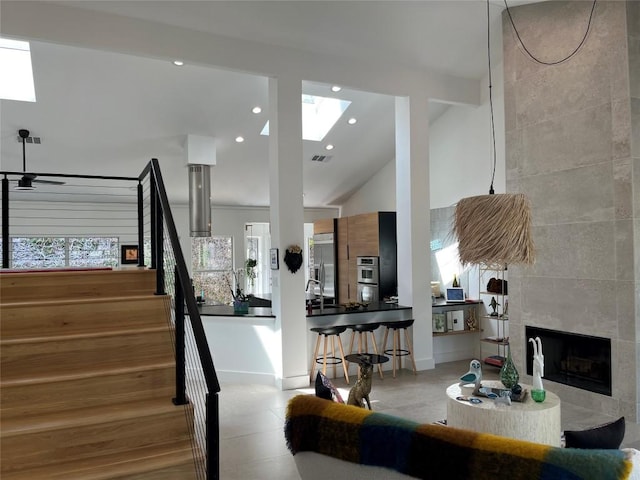 interior space with a tiled fireplace, a skylight, and high vaulted ceiling