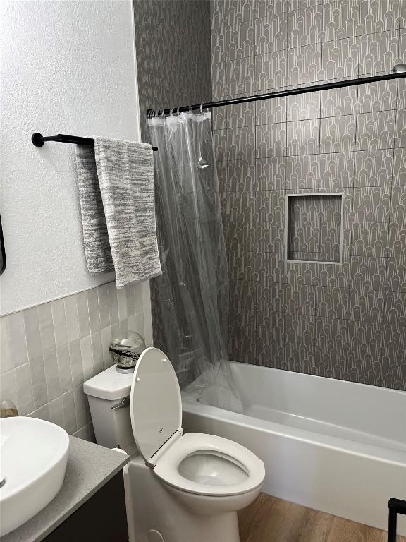 full bathroom with hardwood / wood-style floors, sink, tile walls, tiled shower / bath combo, and toilet