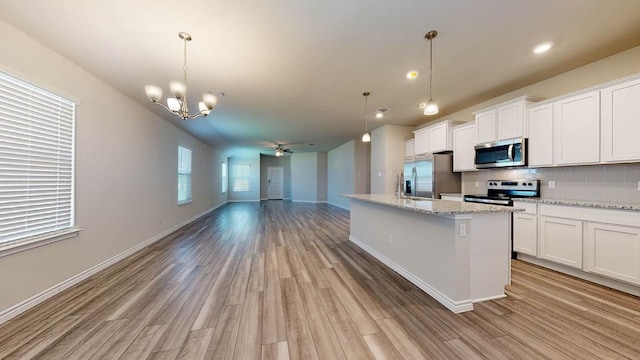 kitchen with an island with sink, pendant lighting, stainless steel appliances, light stone countertops, and white cabinets