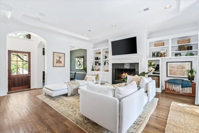 living room with crown molding, built in features, a raised ceiling, and light wood-type flooring