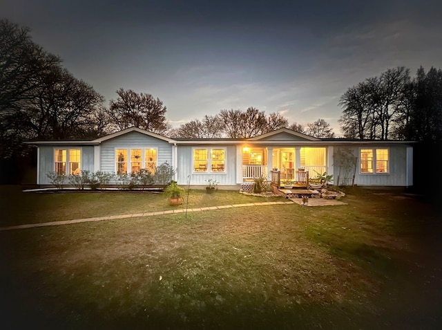 back house at dusk featuring a yard and a porch