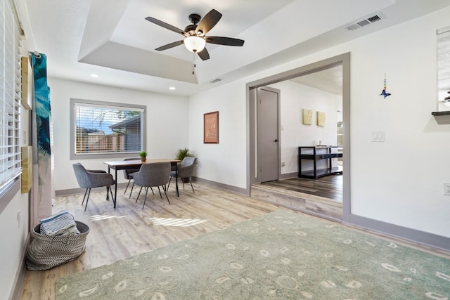 dining space with light hardwood / wood-style floors, a raised ceiling, and ceiling fan