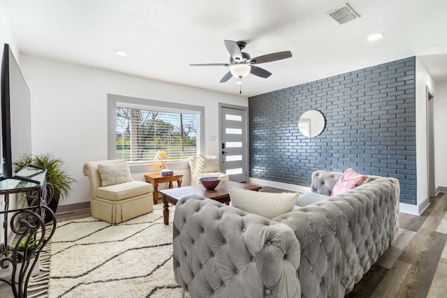 living room featuring hardwood / wood-style flooring, brick wall, and ceiling fan