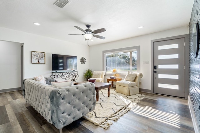 living room with dark wood-type flooring, ceiling fan, and a textured ceiling