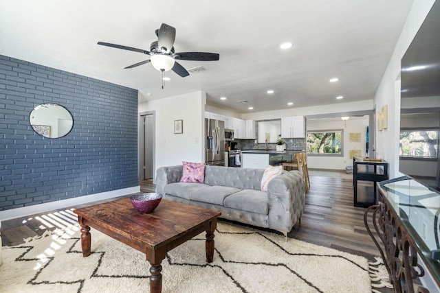 living room featuring hardwood / wood-style flooring, brick wall, and ceiling fan