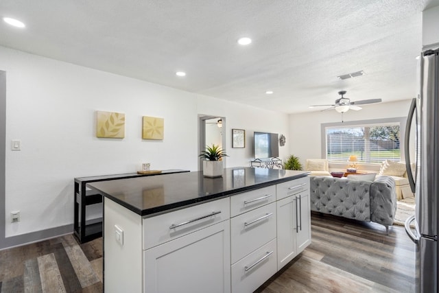 kitchen with white cabinetry, dark wood-type flooring, a kitchen island, and stainless steel refrigerator