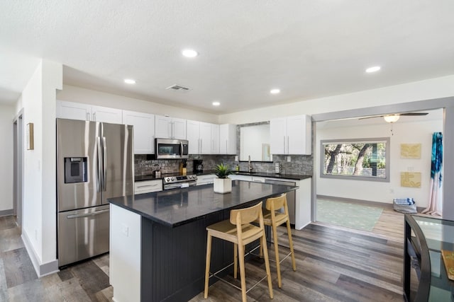 kitchen featuring appliances with stainless steel finishes, tasteful backsplash, white cabinetry, a center island, and dark wood-type flooring