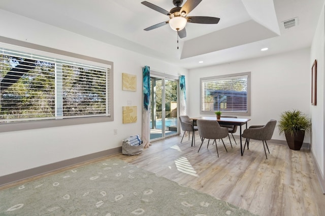 dining space with ceiling fan, light wood-type flooring, and a tray ceiling