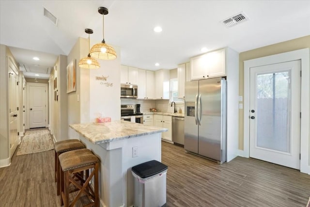 kitchen with white cabinetry, appliances with stainless steel finishes, kitchen peninsula, and hanging light fixtures