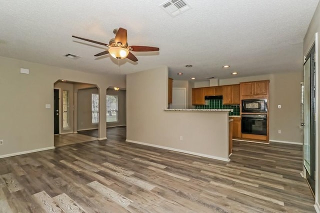 6333 La Mesa St, Leander, TX 78645 - kitchen featuring black appliances, brown cabinets, dark wood-style flooring, arched walkways, and a ceiling fan