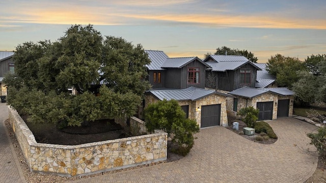 view of front facade featuring an attached garage, a standing seam roof, metal roof, stone siding, and decorative driveway