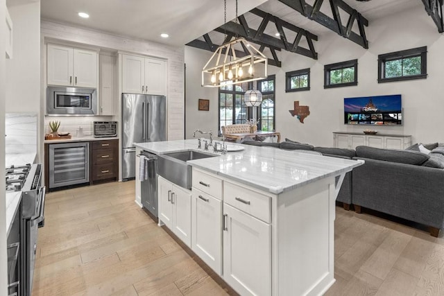 kitchen with appliances with stainless steel finishes, pendant lighting, white cabinetry, sink, and a kitchen island with sink