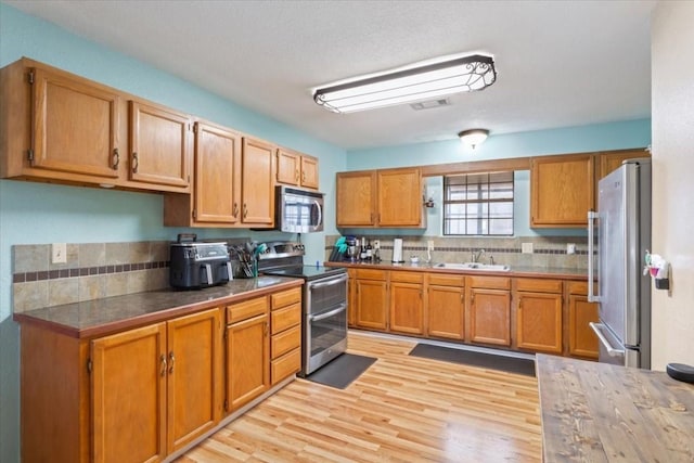 kitchen with appliances with stainless steel finishes, sink, and light hardwood / wood-style flooring