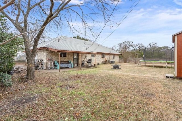 back of property featuring a yard, a patio, a fire pit, and a trampoline