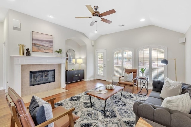 living room featuring ceiling fan, lofted ceiling, a tile fireplace, and light wood-type flooring