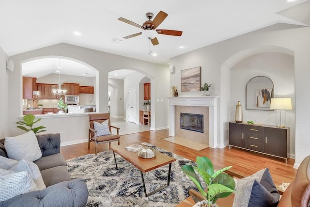 living room featuring lofted ceiling, a tiled fireplace, ceiling fan with notable chandelier, and light hardwood / wood-style floors