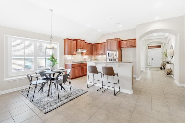 kitchen featuring an inviting chandelier, light tile patterned floors, appliances with stainless steel finishes, an island with sink, and backsplash