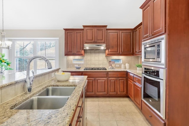 kitchen featuring stainless steel appliances, light stone countertops, sink, and decorative light fixtures