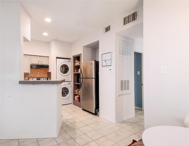 kitchen with stacked washer and clothes dryer, stainless steel fridge, kitchen peninsula, white cabinets, and backsplash