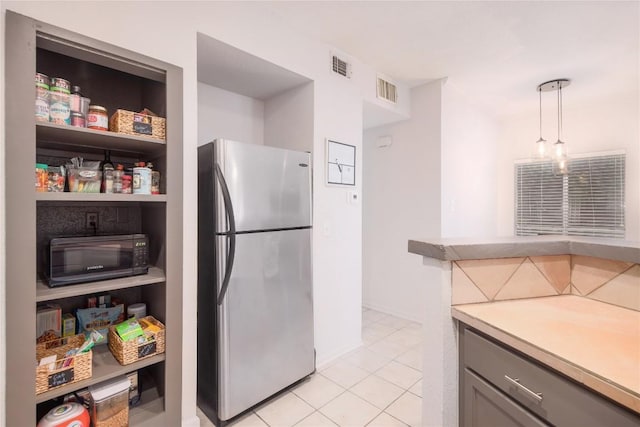 kitchen featuring stainless steel refrigerator, light tile patterned flooring, hanging light fixtures, and gray cabinetry