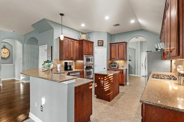 kitchen with sink, light stone counters, a center island, kitchen peninsula, and stainless steel appliances