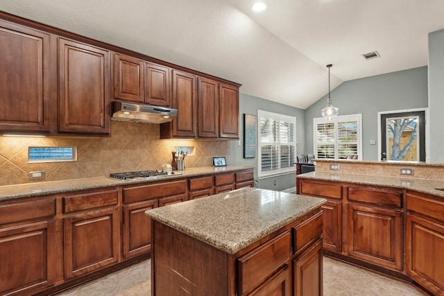 kitchen featuring pendant lighting, a center island, light stone countertops, stainless steel gas cooktop, and vaulted ceiling