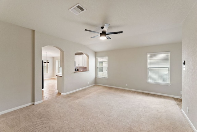 unfurnished room featuring ceiling fan, arched walkways, light carpet, visible vents, and vaulted ceiling