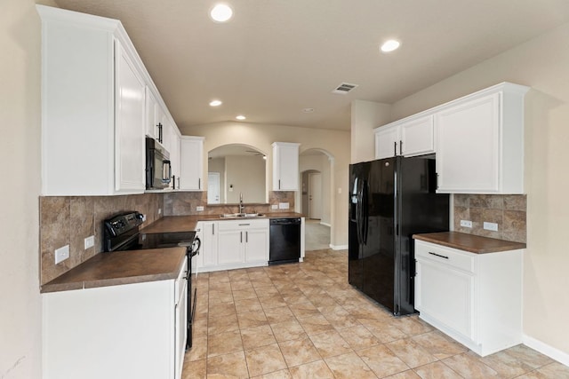 kitchen with arched walkways, black appliances, dark countertops, and a sink