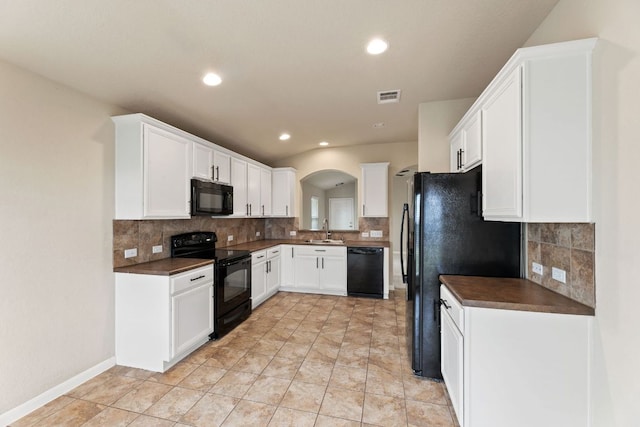 kitchen featuring dark countertops, visible vents, white cabinets, a sink, and black appliances