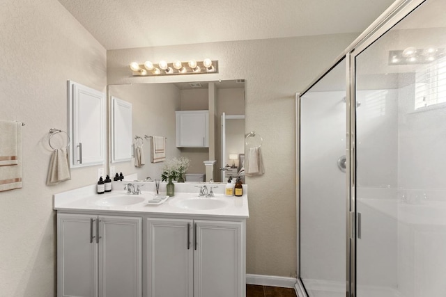 bathroom featuring double vanity, a shower stall, a sink, and a textured wall