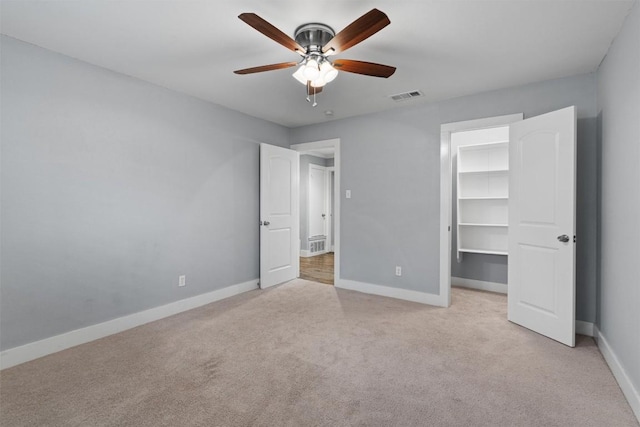 unfurnished bedroom with a walk in closet, light colored carpet, a closet, and ceiling fan