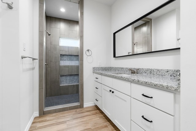 bathroom featuring wood-type flooring, tiled shower, and vanity