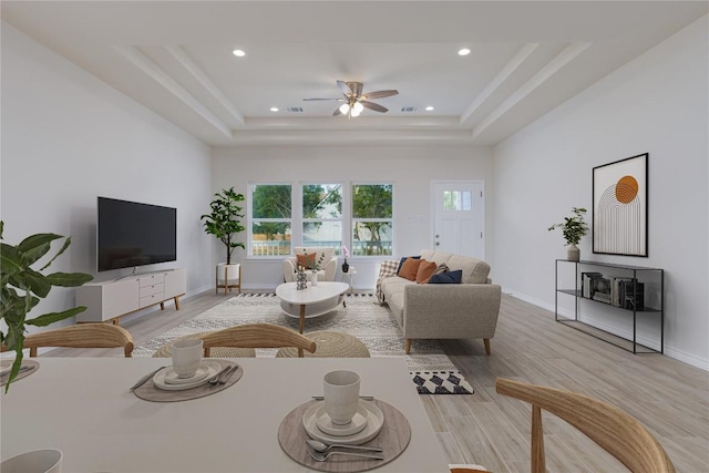 living room featuring ceiling fan, a raised ceiling, and light wood-type flooring