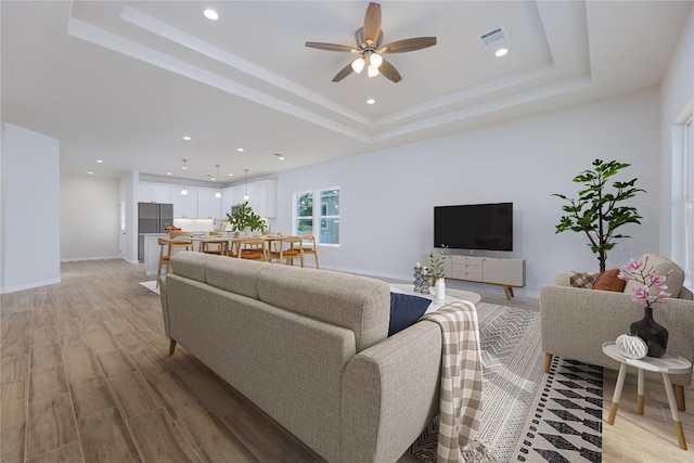 living room featuring a raised ceiling, ceiling fan, and light wood-type flooring