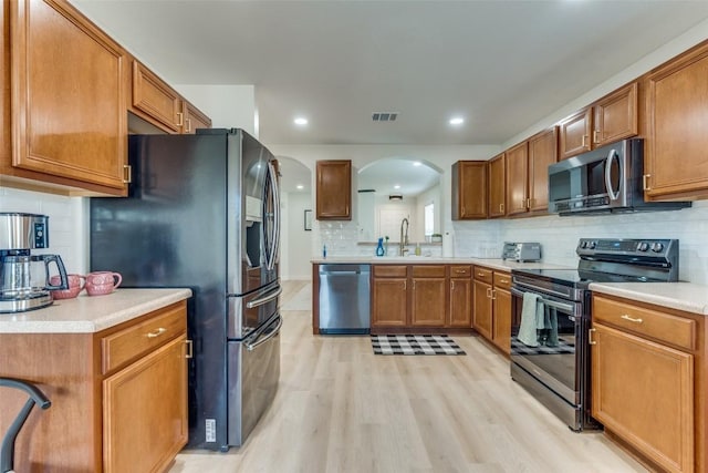 kitchen featuring decorative backsplash, stainless steel appliances, sink, and light hardwood / wood-style flooring