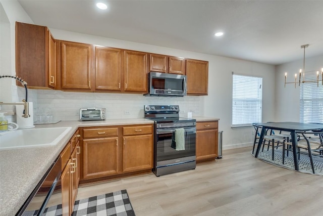 kitchen featuring sink, light wood-type flooring, appliances with stainless steel finishes, pendant lighting, and decorative backsplash