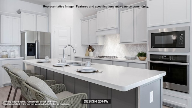 kitchen with sink, a center island with sink, appliances with stainless steel finishes, a kitchen breakfast bar, and white cabinets