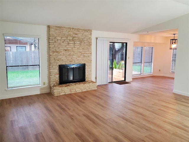 unfurnished living room featuring a wealth of natural light, a stone fireplace, hardwood / wood-style floors, and lofted ceiling