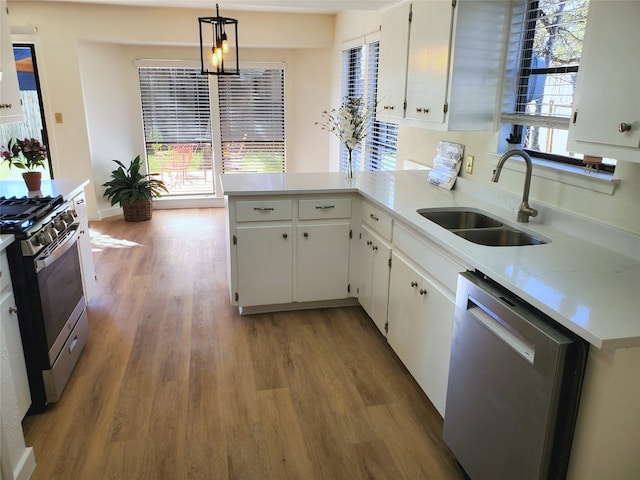 kitchen featuring light wood finished floors, light countertops, appliances with stainless steel finishes, a peninsula, and a sink