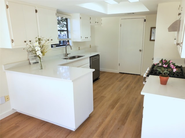 kitchen with a sink, light wood-style floors, appliances with stainless steel finishes, a peninsula, and light countertops