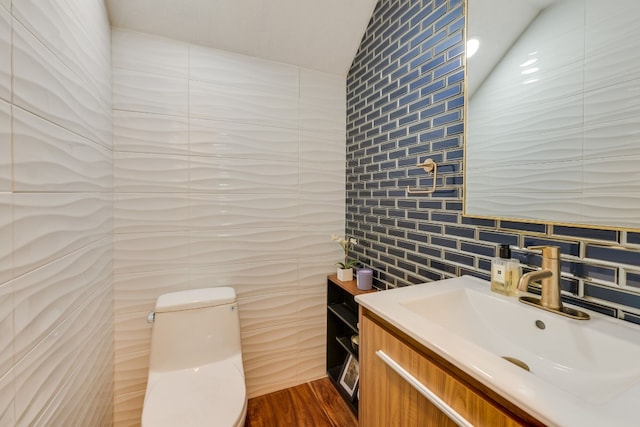 bathroom with vaulted ceiling, wood-type flooring, tile walls, vanity, and toilet