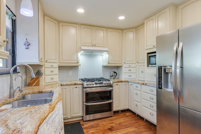 kitchen featuring sink, stainless steel appliances, cream cabinetry, and light stone countertops