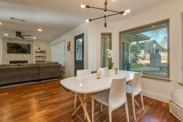 dining space with a high end fireplace, ceiling fan with notable chandelier, and dark hardwood / wood-style flooring