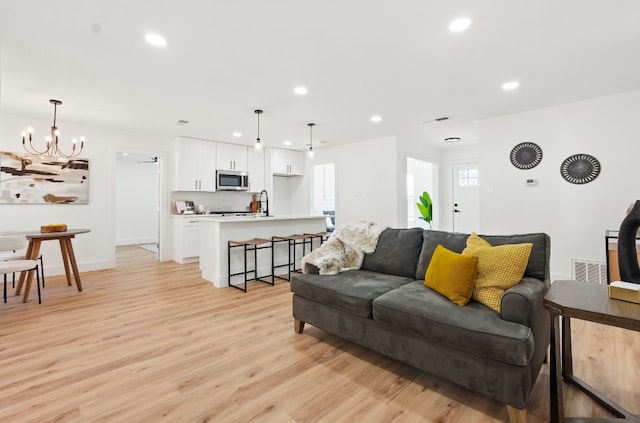 living room with sink, a notable chandelier, and light hardwood / wood-style flooring