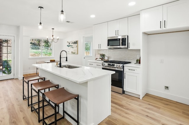 kitchen featuring sink, stainless steel appliances, an island with sink, white cabinets, and decorative light fixtures