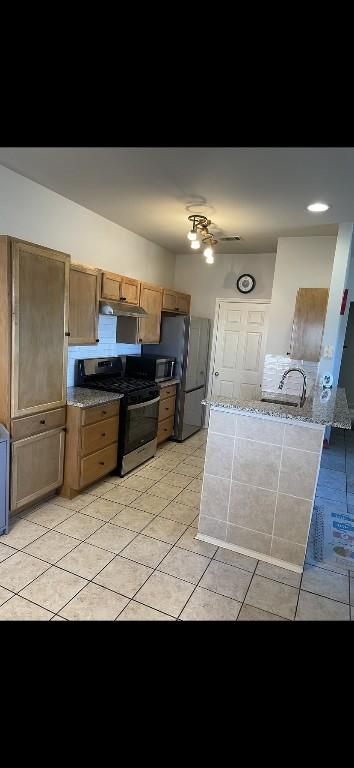 kitchen featuring stone counters, light tile patterned floors, fridge with ice dispenser, and stainless steel gas range oven