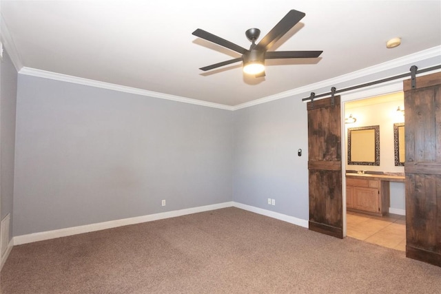 unfurnished bedroom with ornamental molding, light colored carpet, ceiling fan, a barn door, and ensuite bath