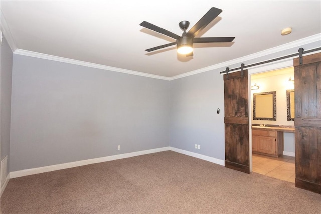 unfurnished bedroom with a barn door, ensuite bath, crown molding, baseboards, and light colored carpet