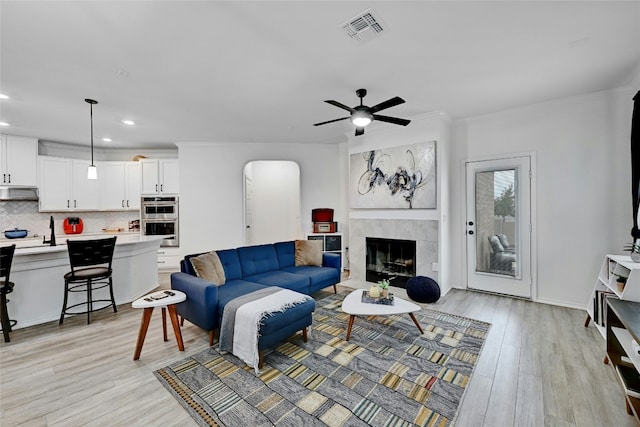 living room featuring a tiled fireplace, ornamental molding, and light hardwood / wood-style floors